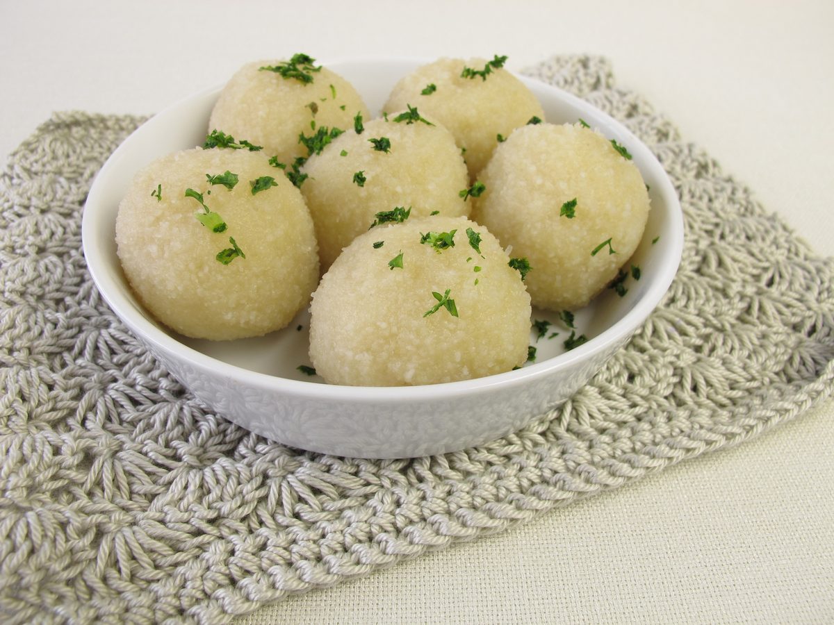 Kartoffelklöße, round German potato dumplings sprinkled with herbs, in a white bowl
