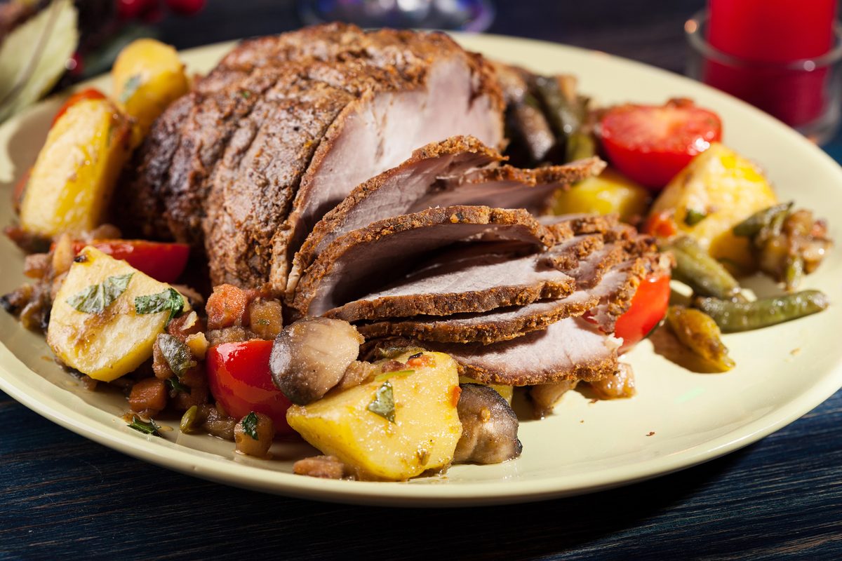Sliced roast pork with roasted vegetables on a holiday platter