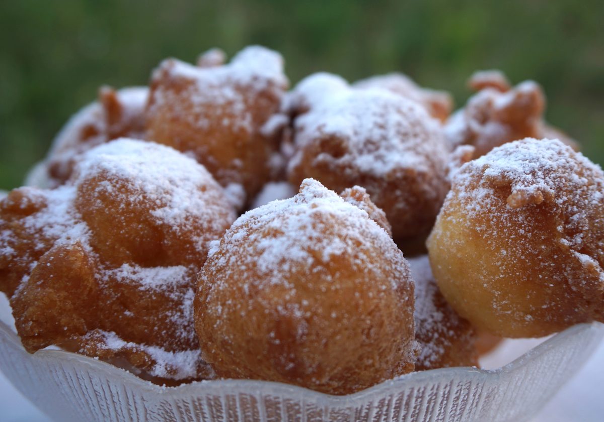 Fritule, small fried dough balls dusted with powdered sugar, in a glass bowl