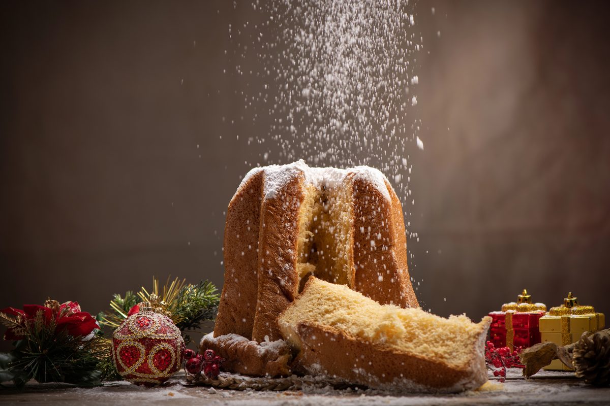 Star-shaped pandoro being dusted with powdered sugar beside wrapped gifts