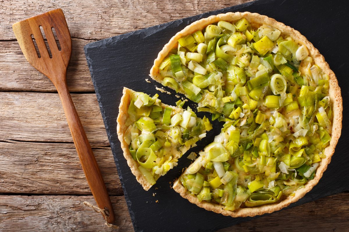 Leek and cheese tart with a slice cut, on a slate board