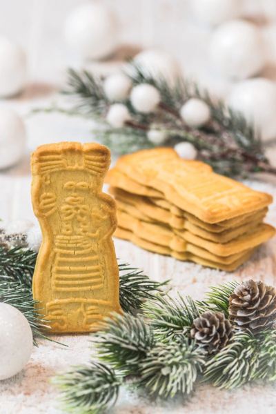 Spekulatius spiced shortcrust cookies stacked beside a figure-shaped cookie, with fir branches and pine cones