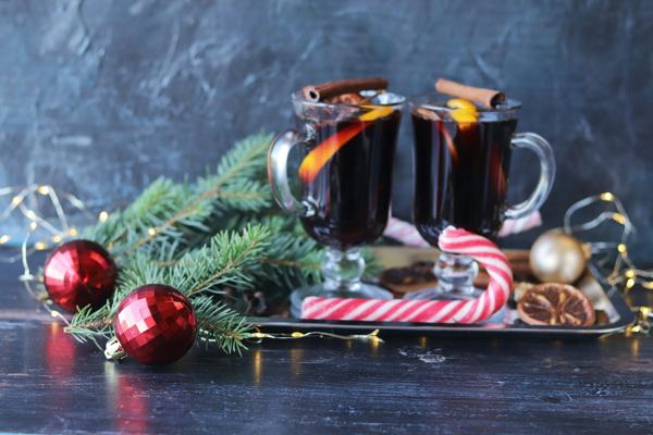 Two mugs of Glühwein mulled wine with spices and Christmas ornaments on a dark table
