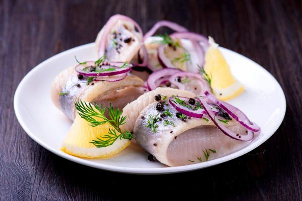 Pickled herring with onion, pepper and herbs on a white plate