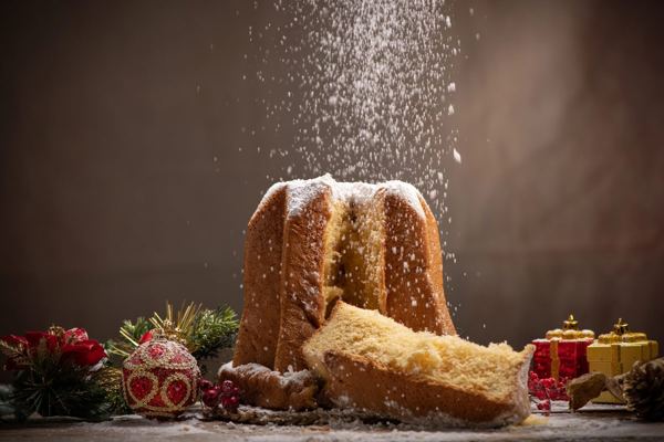 Star-shaped pandoro being dusted with powdered sugar beside wrapped gifts