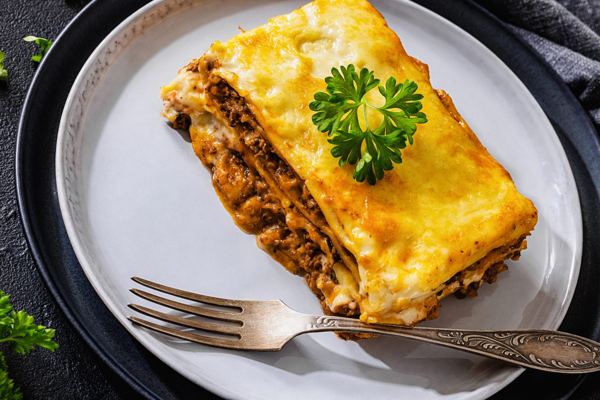 Slice of baked lasagna with meat ragù and melted cheese on a plate
