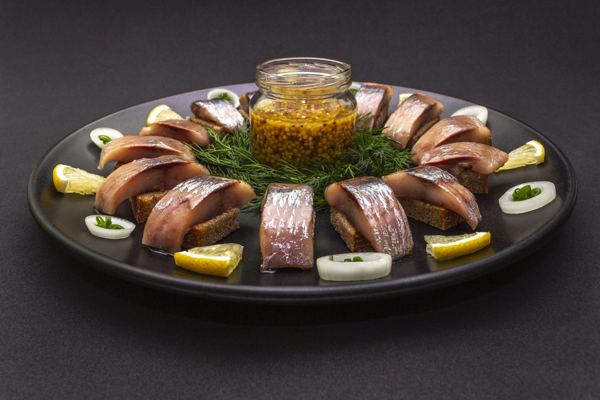 Platter of herring pieces with a bowl of mustard sauce