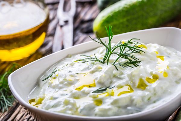Bowl of tzatziki with dill and olive oil, next to a cucumber
