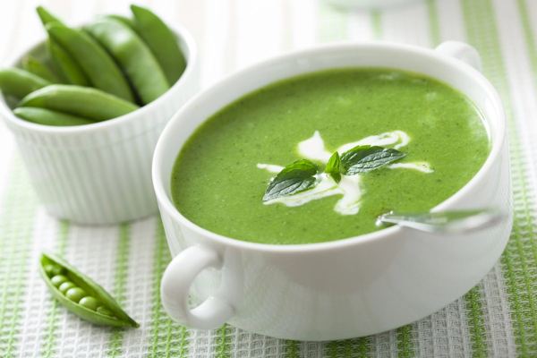 Bowl of green pea soup with a swirl of cream and fresh peas